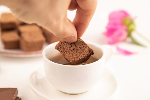Chocolate marshmallow with cup of coffee with hand on white wooden background. side view, close up,