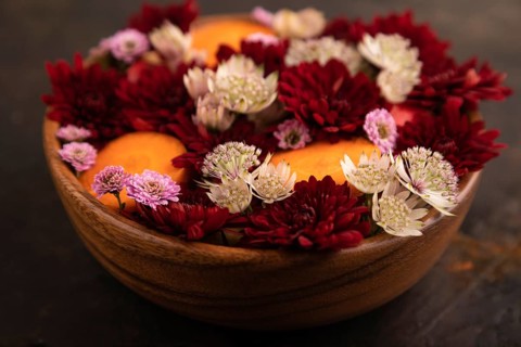 Wooden bowl with carrot slices and red Chrysanthemum flowers, Astrantia flowers, flower salad on