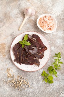 Armenian Basturma dried meat on plate with pepper and herbs on brown concrete background. Top view,