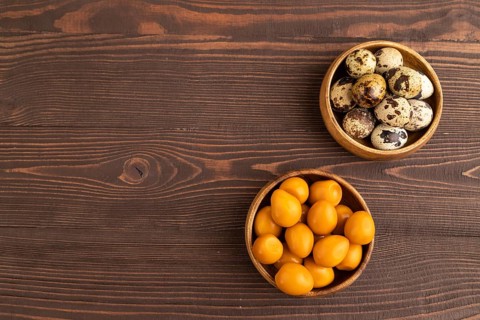 Pile of Smoked Quail eggs in bowl on a brown wooden background. top view, flat lay, copy space