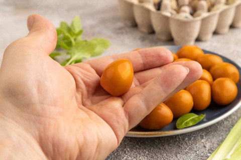 Pile of Smoked Quail eggs on plate with hand on a brown concrete background. side view, close up