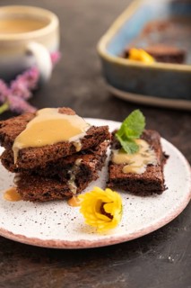 Chocolate brownie with caramel sauce with a cup of coffee on black concrete background. side view,