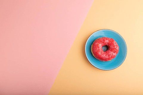Pink Donut with sprinkles on blue ceramic plate on blue and orange pastel paper background, top