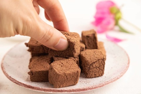 Chocolate marshmallow with cup of coffee with hand on white wooden background. side view, close up,