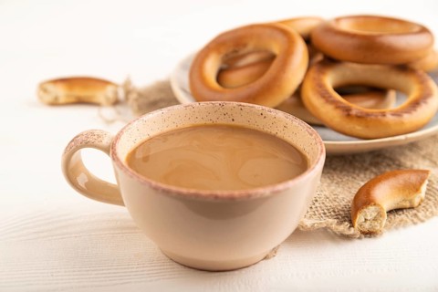 Homemade Ring Bagel with cup of coffee on white wooden background and linen textile. side view,