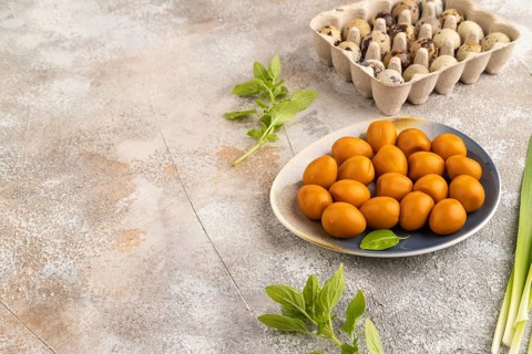 Pile of Smoked Quail eggs on plate on a brown concrete background. side view, copy space