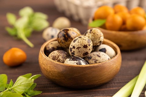 Pile of Smoked Quail eggs in bowl on a brown wooden background. side view, close up, selective