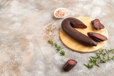 Sujuk sausage on wooden cutting board with pepper and herbs on brown concrete background. Side