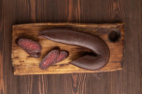Sujuk sausage on wooden cutting board with pepper and herbs on brown wooden background. Top view,