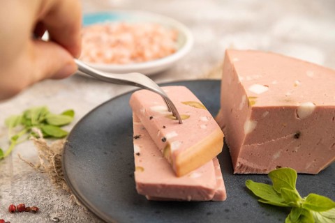 Mortadella sausage with hand on plate with pepper and herbs on brown concrete background and linen