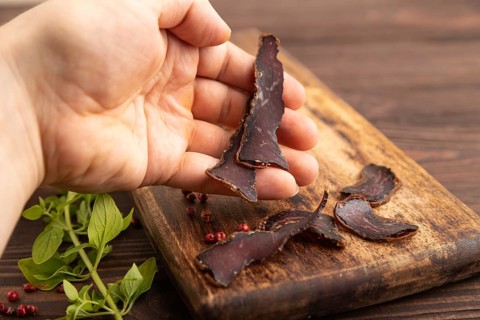 Armenian Basturma dried meat with hand on wooden cutting board with pepper and herbs on brown