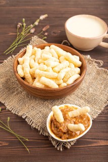 Corn flakes sticks with caramel in wooden bowl on brown wooden background and linen textile. Side