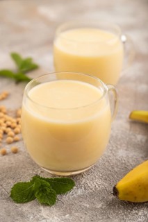 Organic non dairy banana and soy milk in glass on brown concrete background. Vegan healthy food
