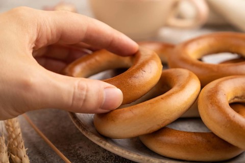 Homemade Ring Bagel with hand with cup of coffee on brown concrete background and linen textile.