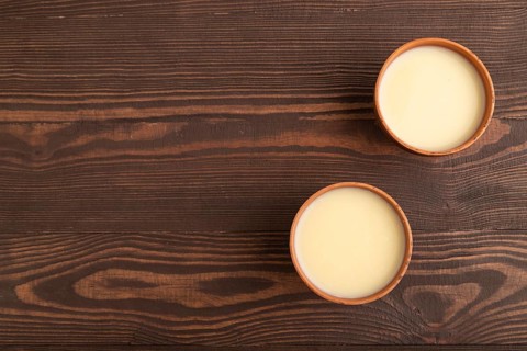 Organic non dairy banana and soy milk in clay cup on brown wooden background. Vegan healthy food