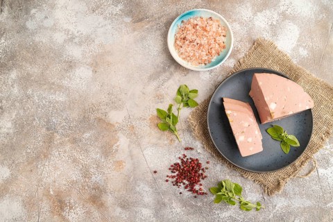 Mortadella sausage on plate with pepper and herbs on brown concrete background and linen textile.