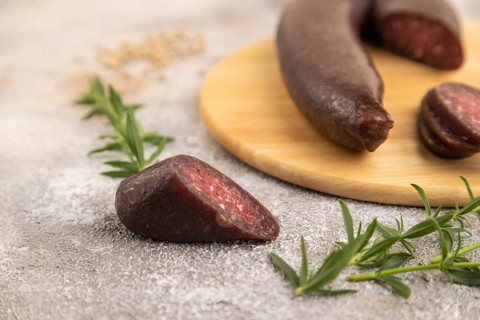 Sujuk sausage on wooden cutting board with pepper and herbs on brown concrete background. Side