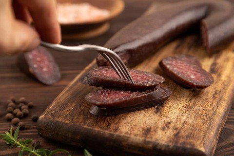 Sujuk sausage with hand on wooden cutting board with pepper and herbs on brown wooden background.