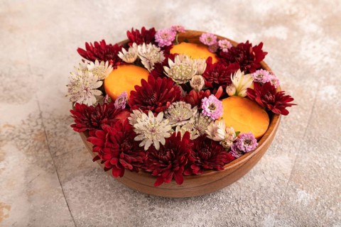 Wooden bowl with carrot slices and red Chrysanthemum flowers, Astrantia flowers, flower salad on