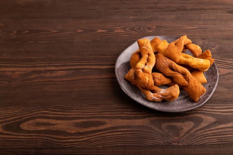 Crunchy biscuit Brushwood cookies sprinkled with powdered sugar on brown wooden background, side