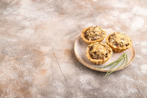Tartlets with meat and cheese on brown concrete background. side view, copy space