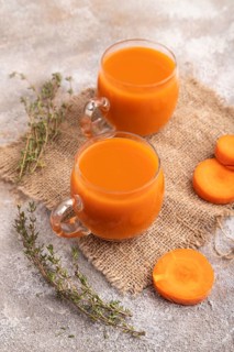 Two glasses with carrot juice, on brown concrete background and linen textile. Diet, healthy eating