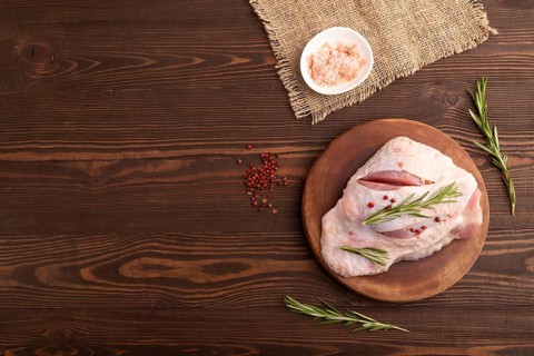 Raw Turkey Thigh with spices and rosemary on cutting board on brown wooden background and linen