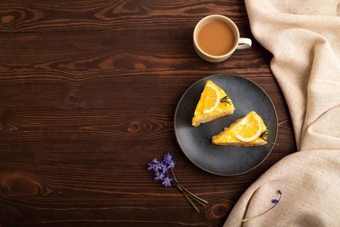 Lemon cake on brown wooden background and linen textile, cup of coffee, top view, flat lay, copy