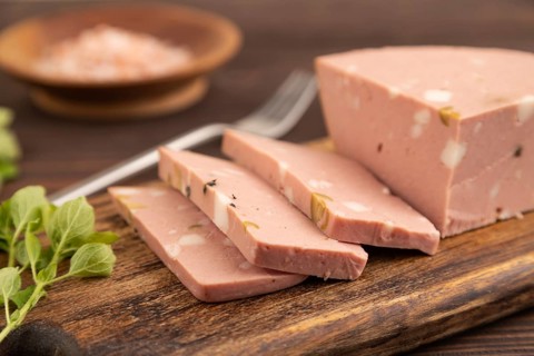 Mortadella sausage on wooden cutting board with pepper and herbs on brown wooden background. Side