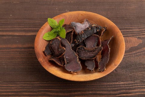 Armenian Basturma dried meat on wooden bowl with pepper and herbs on brown wooden background. Side