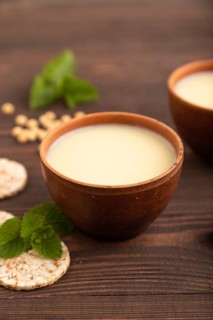 Organic non dairy banana and soy milk in clay cup on brown wooden background. Vegan healthy food