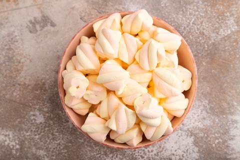 Orange and pink marshmallow in ceramic bowl on brown concrete background, top view, flat lay, copy