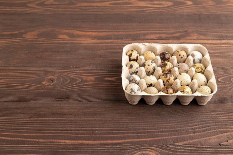 Pile of raw Quail eggs on brown wooden background. side view, flat lay, copy space