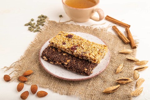 Granola bars with caramel, nuts, flakes in ceramic plate on white wooden background, beige linen