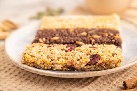 Granola bars with caramel, nuts, flakes in ceramic plate on brown concrete background, beige linen