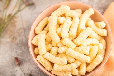 Corn flakes sticks with caramel in ceramic bowl on gray concrete background and orange linen