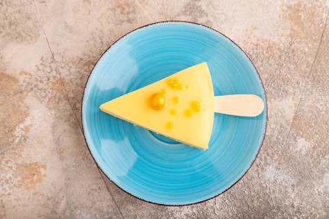 Yellow Cake pop with sprinkles on blue ceramic plate on brown concrete background, top view, flat