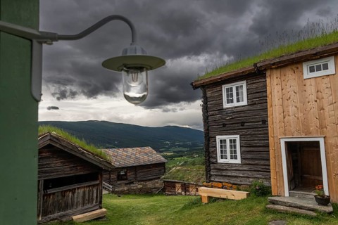 Holzhäuser mit Grasdächern in einer weiten Landschaft, historischer Bauernhof und Pilgerunterkunft