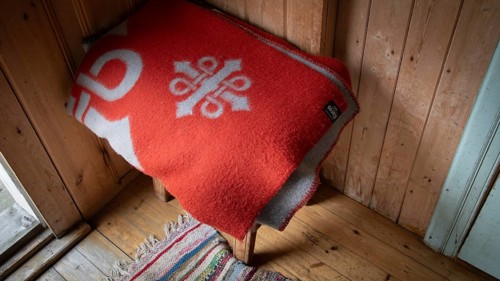 Rote Wolldecke mit Olavsweg-Symbol liegt auf einem Holzschemel, historischer Bauernhof und