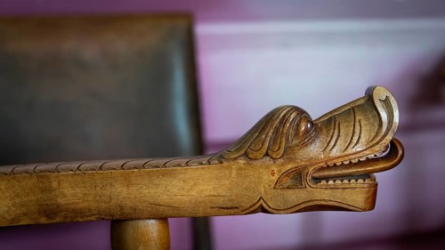 Detailreiche Schnitzerei eines Drachenkopfes an der Armlehne eines Holzstuhls, historischer