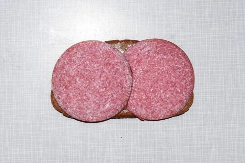 Top shot of a slice of bread smeared with margarine and topped with salami on a white Resopal plate