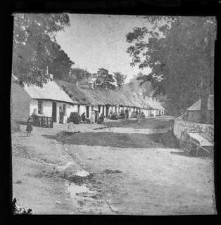 Prosperous looking people sitting outside thatched workers' one storey whitewashed cottages,