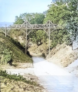 Colourised magic lantern slide of footbridge crossing the road at Wilford Hollows, Bromeswell,