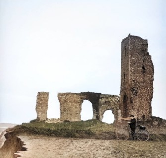 Colorised magic lantern slide of boy with bicycle standing by ruins of All Saints church, Dunwich,