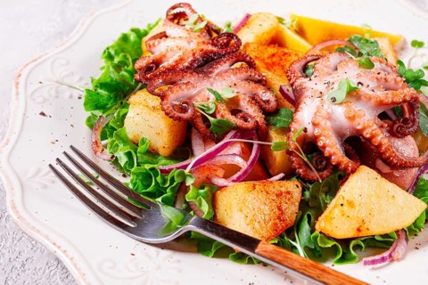 Grilled octopus with baked potatoes and fresh herbs, on a decorative light plate, homemade, no