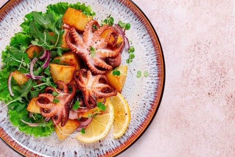 Grilled octopus with baked potatoes and fresh herbs, on a decorative plate, homemade