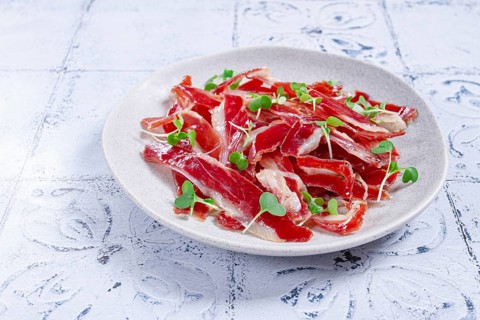 Ham of duck breast, dried duck fillet, with microgreens, plate, on a tiled table