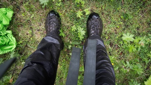 Blick auf nasse Wanderschuhe, Wanderhose und Gras von oben, regnerisches Wetter, Pilgerweg