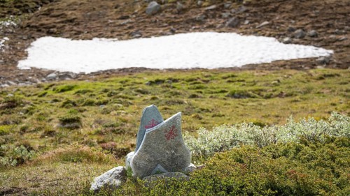 Olavskreuz auf Steinen, Wegmarkierung für Pilger, dahinter kleines Schneefeld in bergiger
