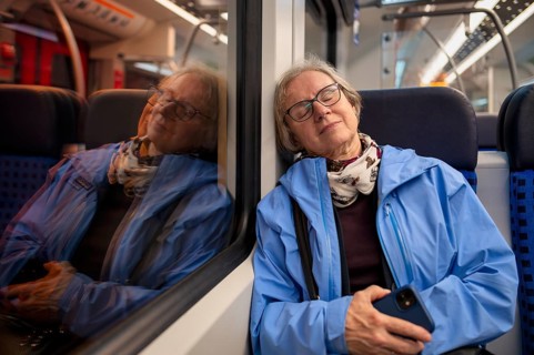 Innenaufnahme, ältere Frau, Brille, sitzt in S-Bahn, Zug, schläft, erschöpft, träumt, Smartphone,